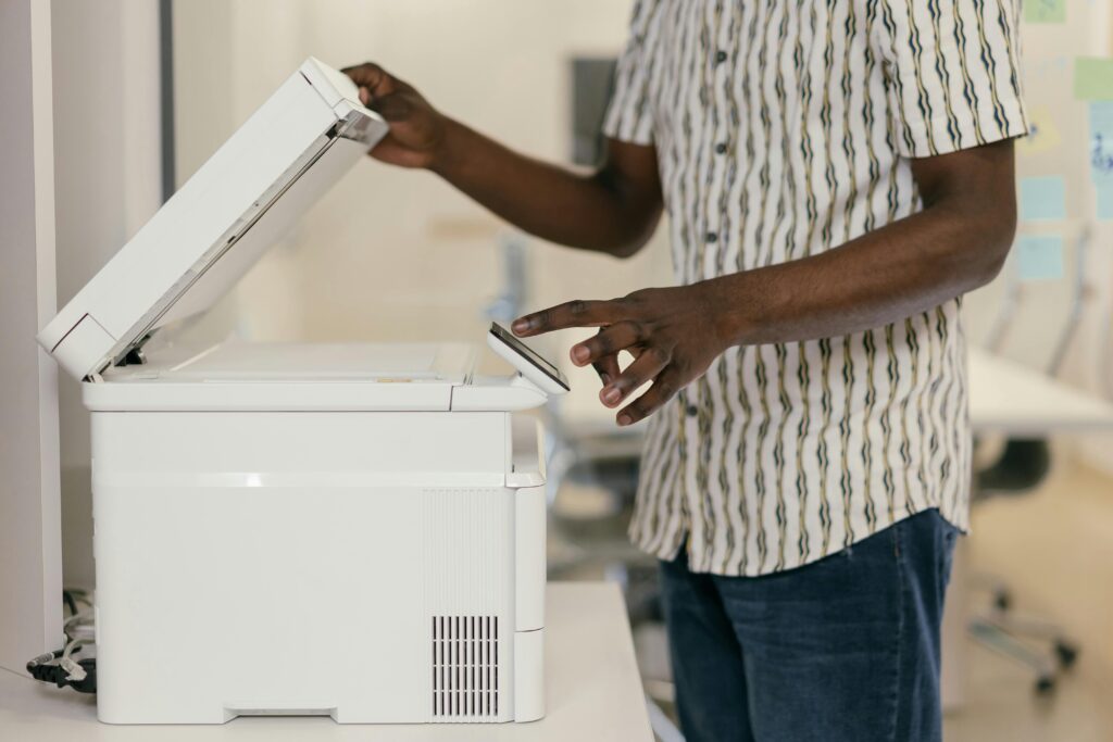 Person operating photocopier in modern office setting, engaging with technology.